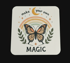 Coaster with butterfly design, rainbow, and text 'make your own magic' on a black background