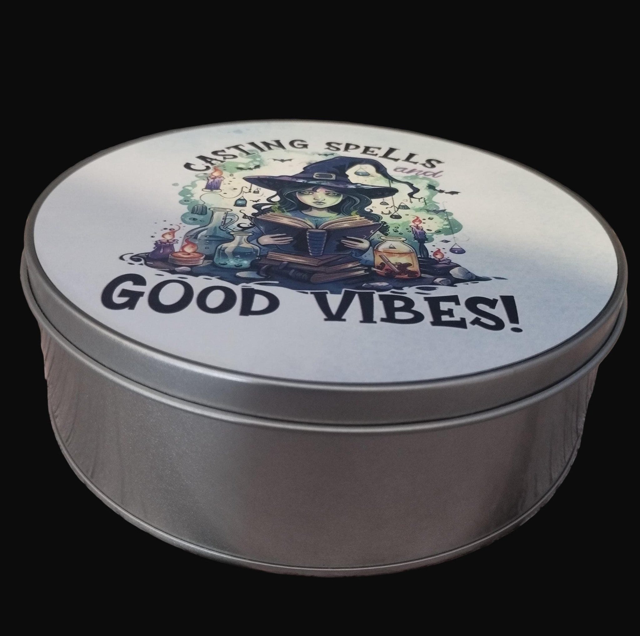 Round metal tin with a witch illustration and 'Casting Spells for Good Vibes!' text on a wooden surface.