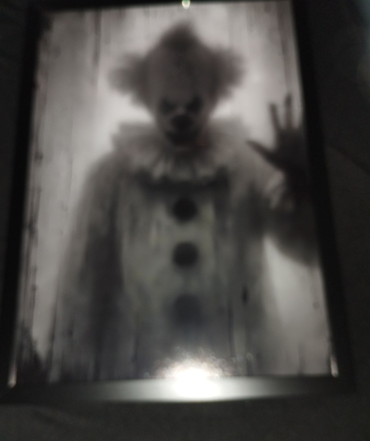 Ghostly monochrome clown behind misty glass with one hand raised against the pane