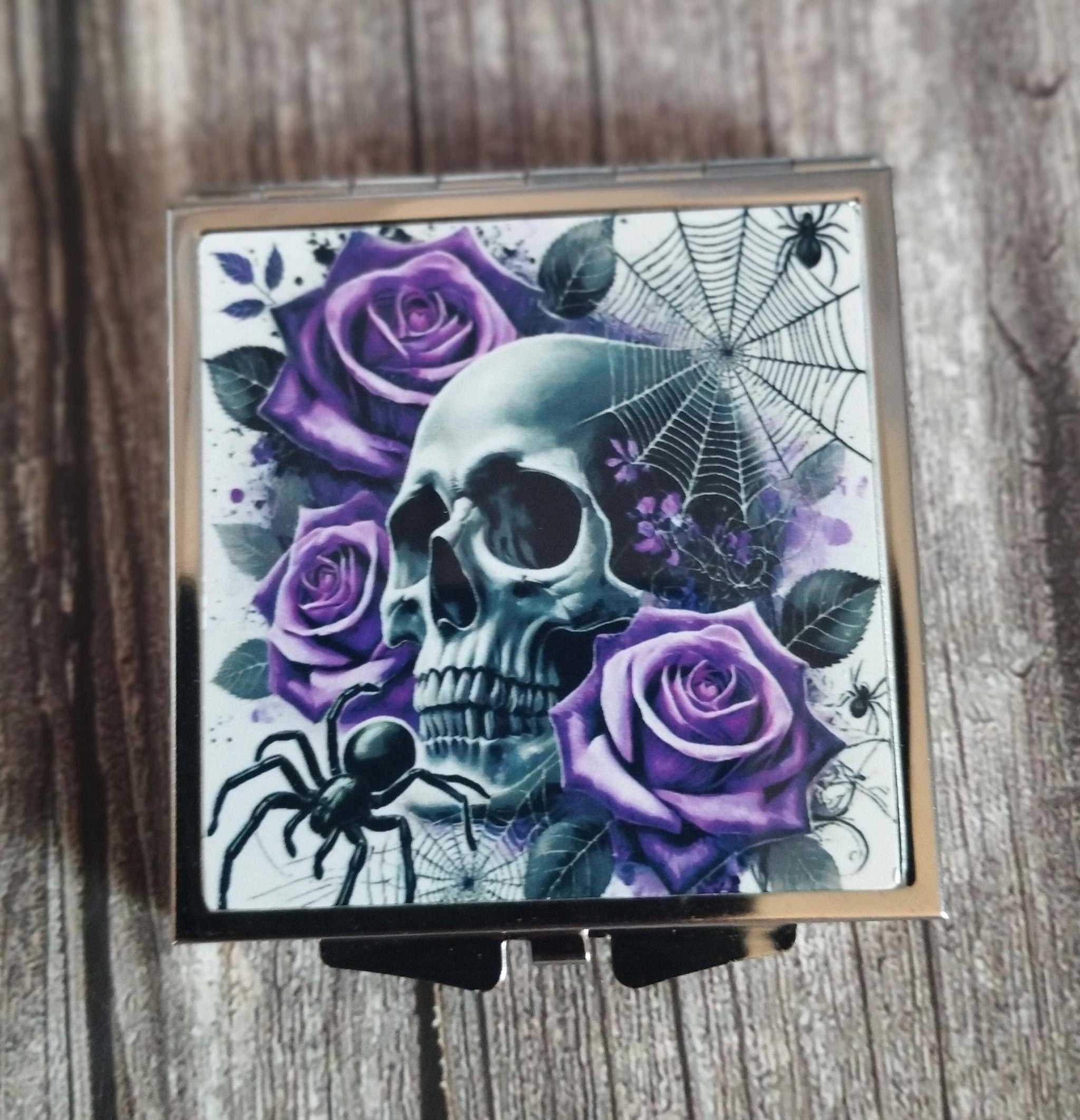 Compact mirror with skull and purple roses design on a wooden surface