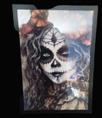Framed artwork of a person with a skull makeup design surrounded by pumpkins.