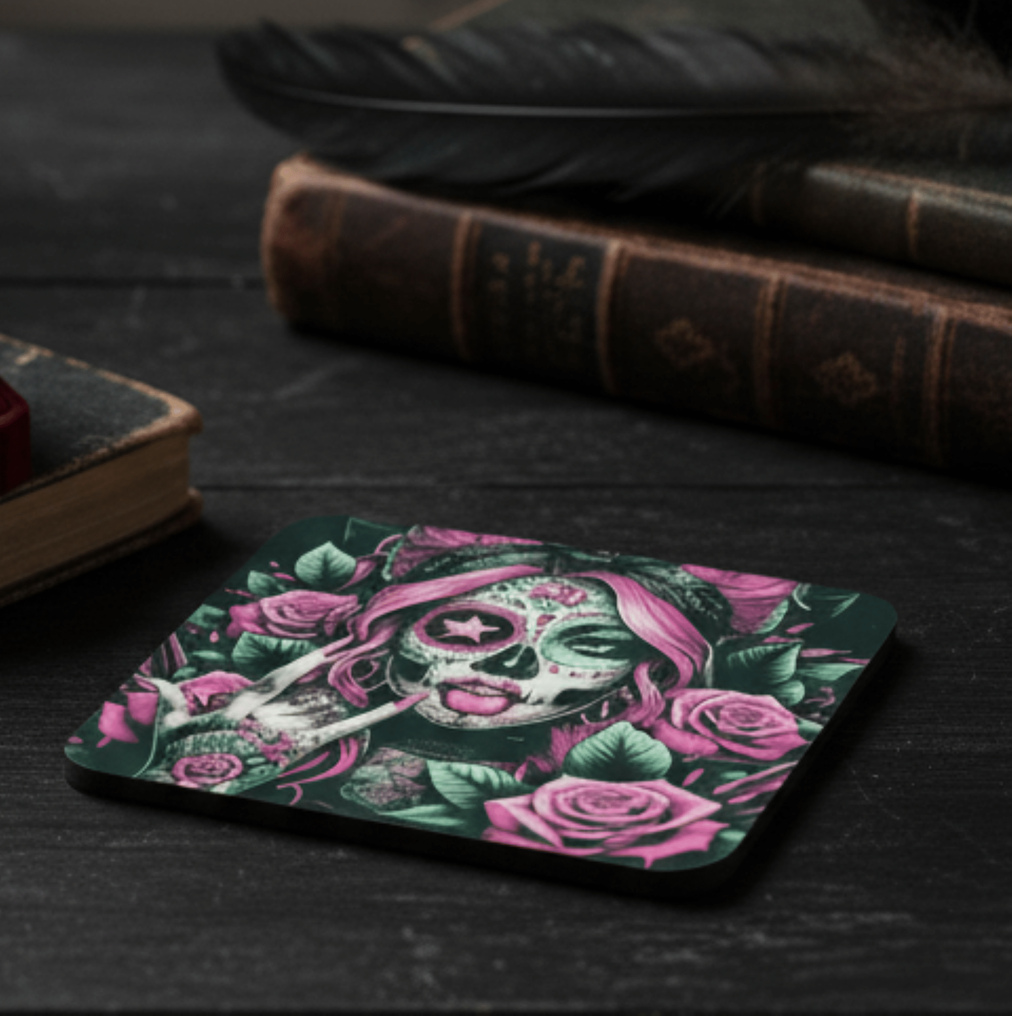 Coaster with a skull and floral design on a dark surface with books and feathers.