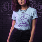 Person wearing a light blue t-shirt with a graphic and text against a dark brick wall.