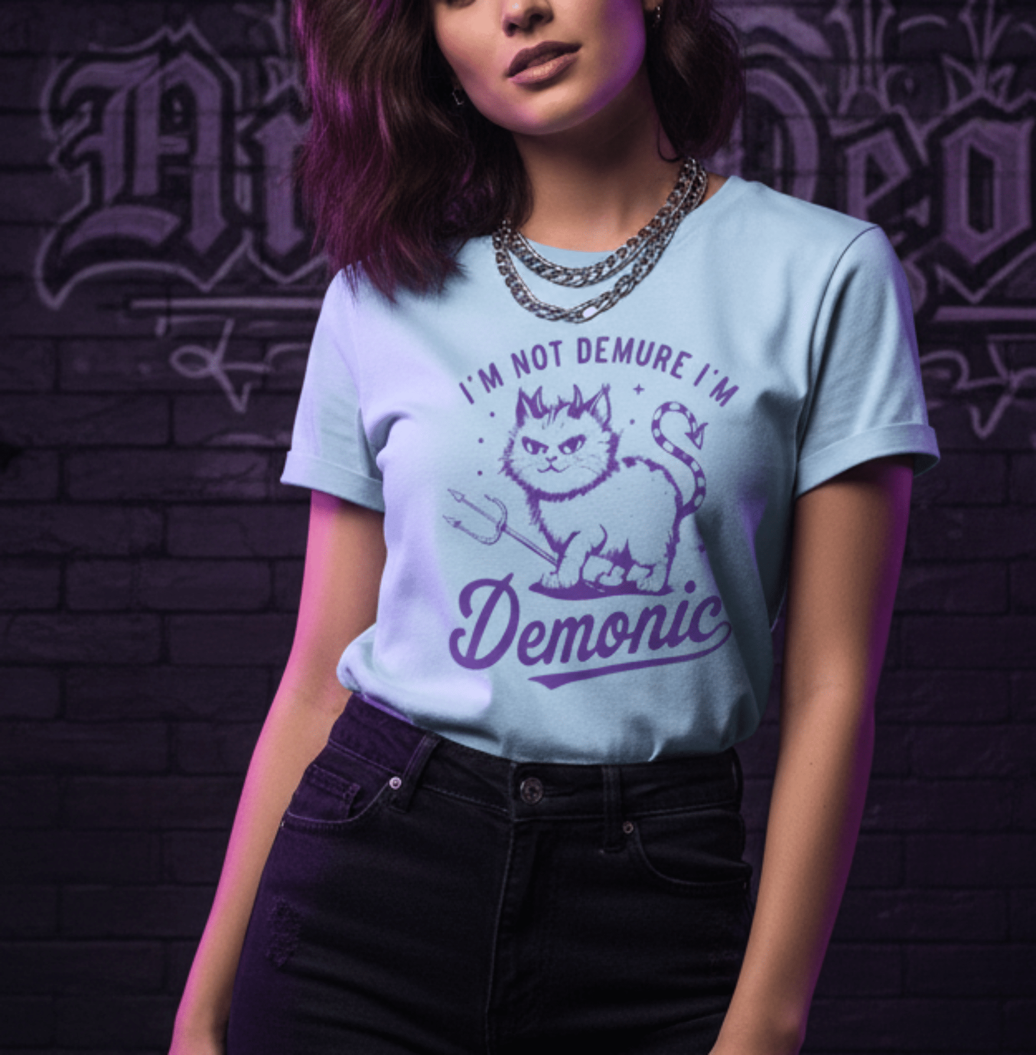 Person wearing a light blue t-shirt with a graphic and text against a dark brick wall.