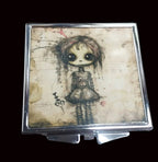 Compact mirror with a gothic-style illustration of a doll on a wooden surface