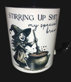 Mug with witch illustration and text 'Stirring up shit, my special brew' on a dark surface.