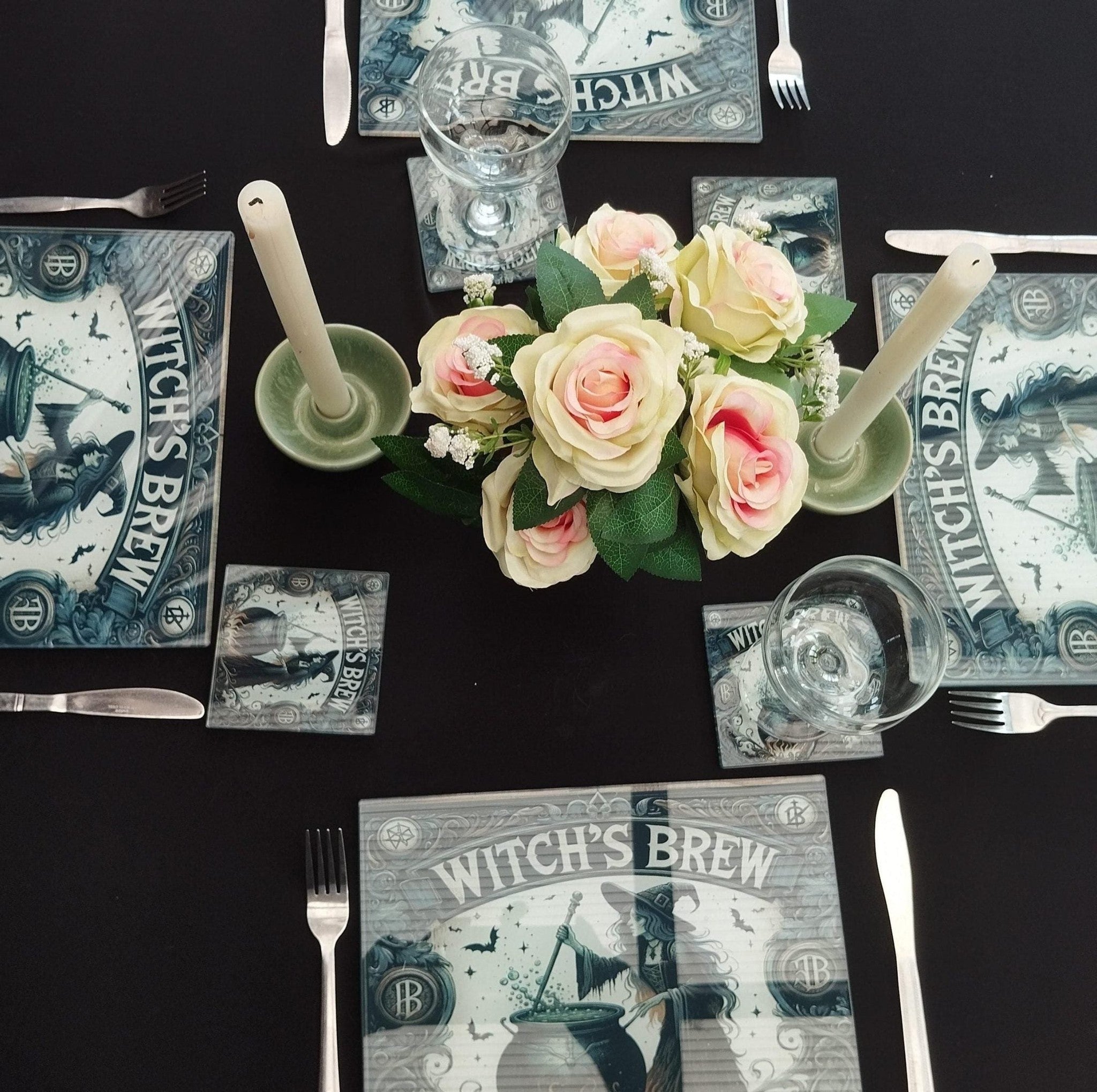 Table setting with floral centerpiece, 'Witch's Brew' themed coasters, and glasses on a black surface.