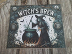 Decorative sign with a witch and pot of brew on a wooden surface