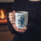 A person in a dark cable-knit sweater holds a white ceramic mug with a blue and black skull graphic decorated with roses and butterflies, with the words 'Beautiful CRAZY' printed on it. The background shows a warm, blurred fireplace.