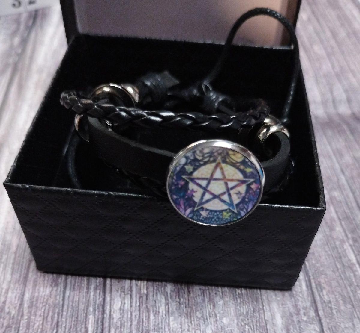Black layered pentagram bracelet with silver-tone details on a wooden background