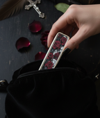 Hand holding a phone case with rose design on a dark surface with feathers and rose petals.