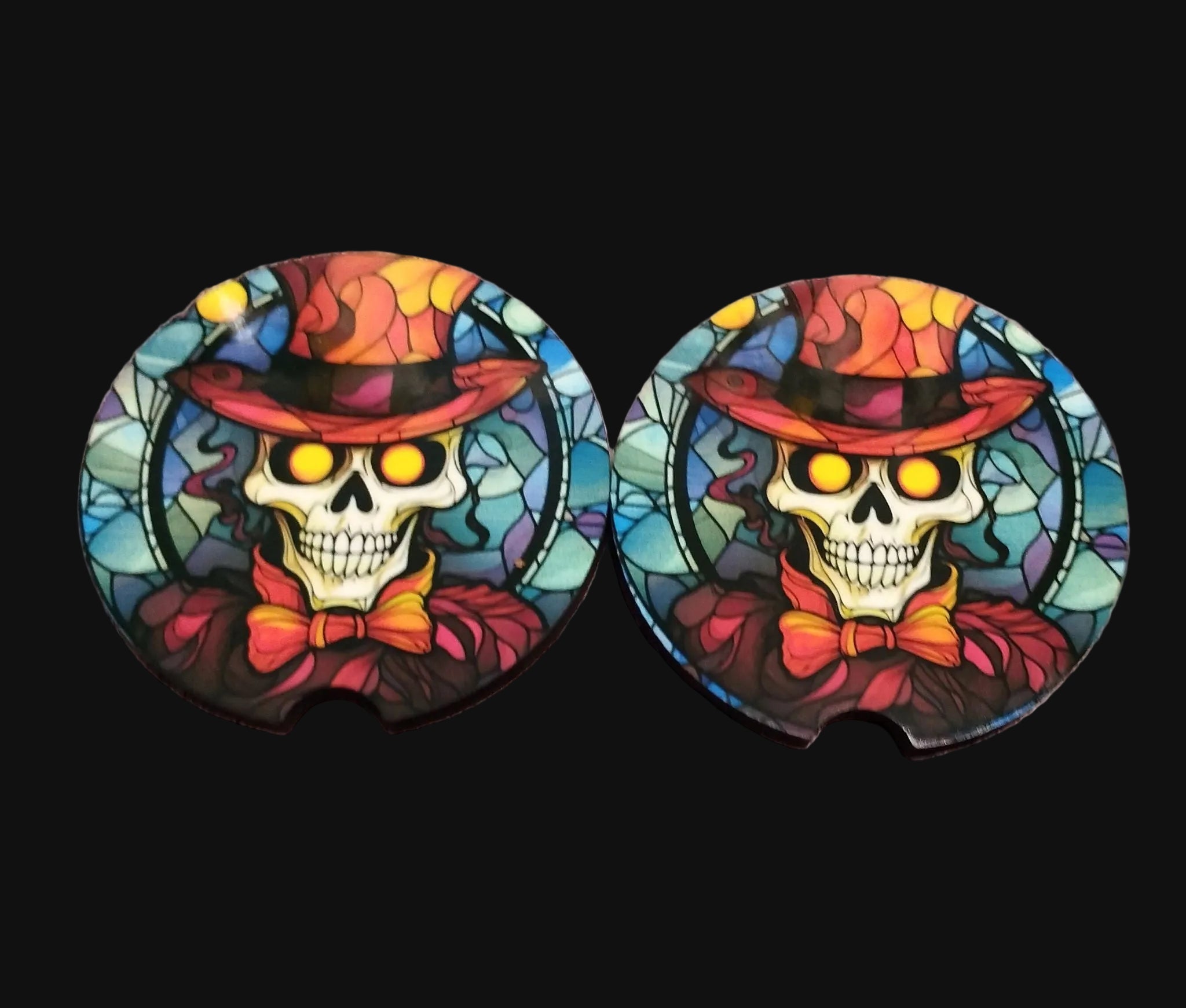 Two colorful skull coasters with hats and bow ties on a wooden surface
